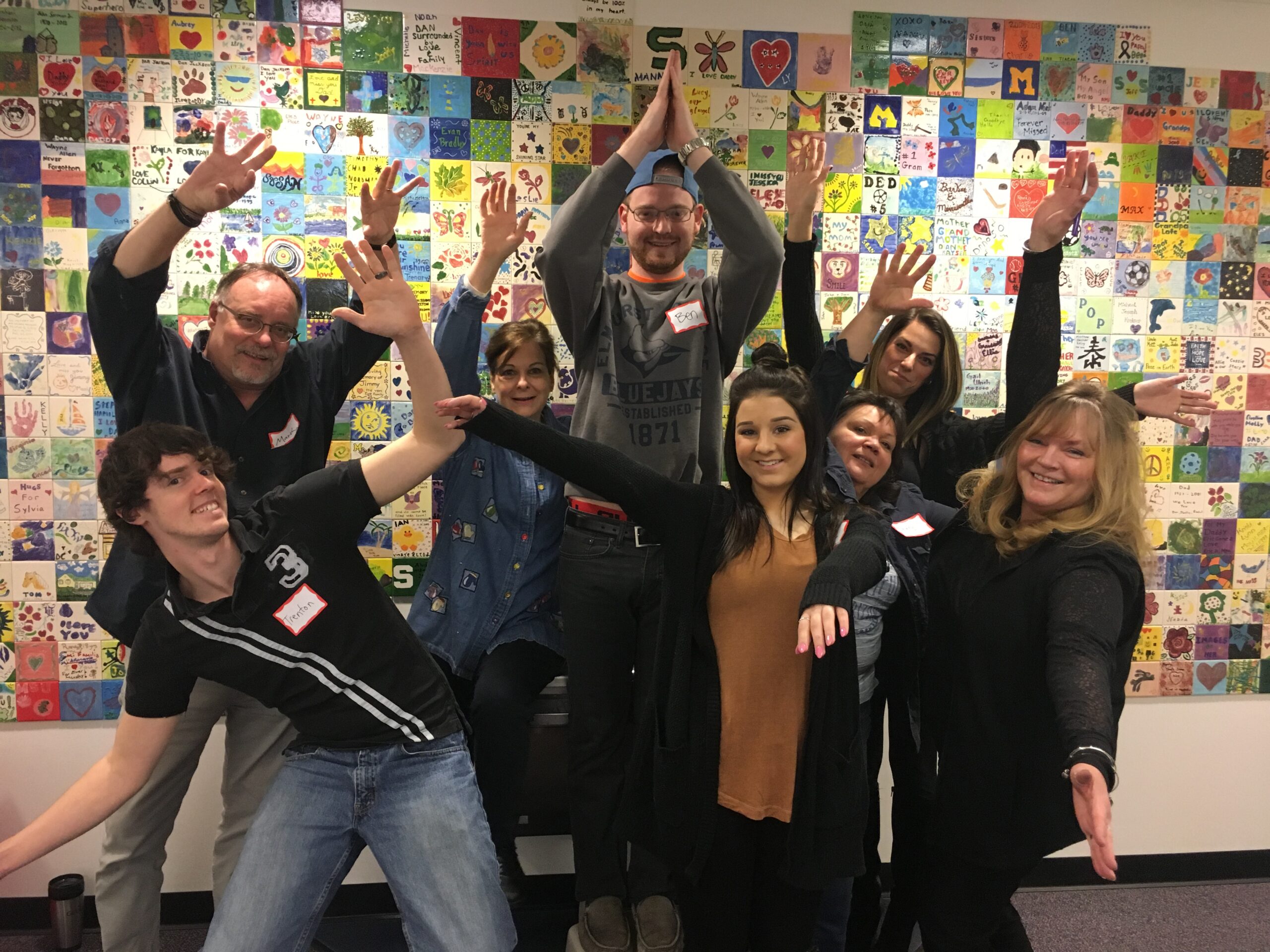 Volunteers posing in front of the painted tiles at Ele's Place.